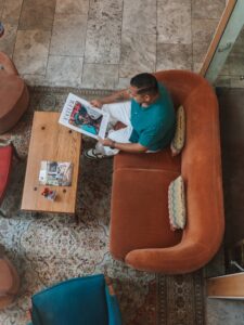 Man in a Teal Shirt Sits on an Orange Curved Sofa Reading a Magazine at a Wooden Coffee Table in a Living Room with a Patterned Rug Oude Werf