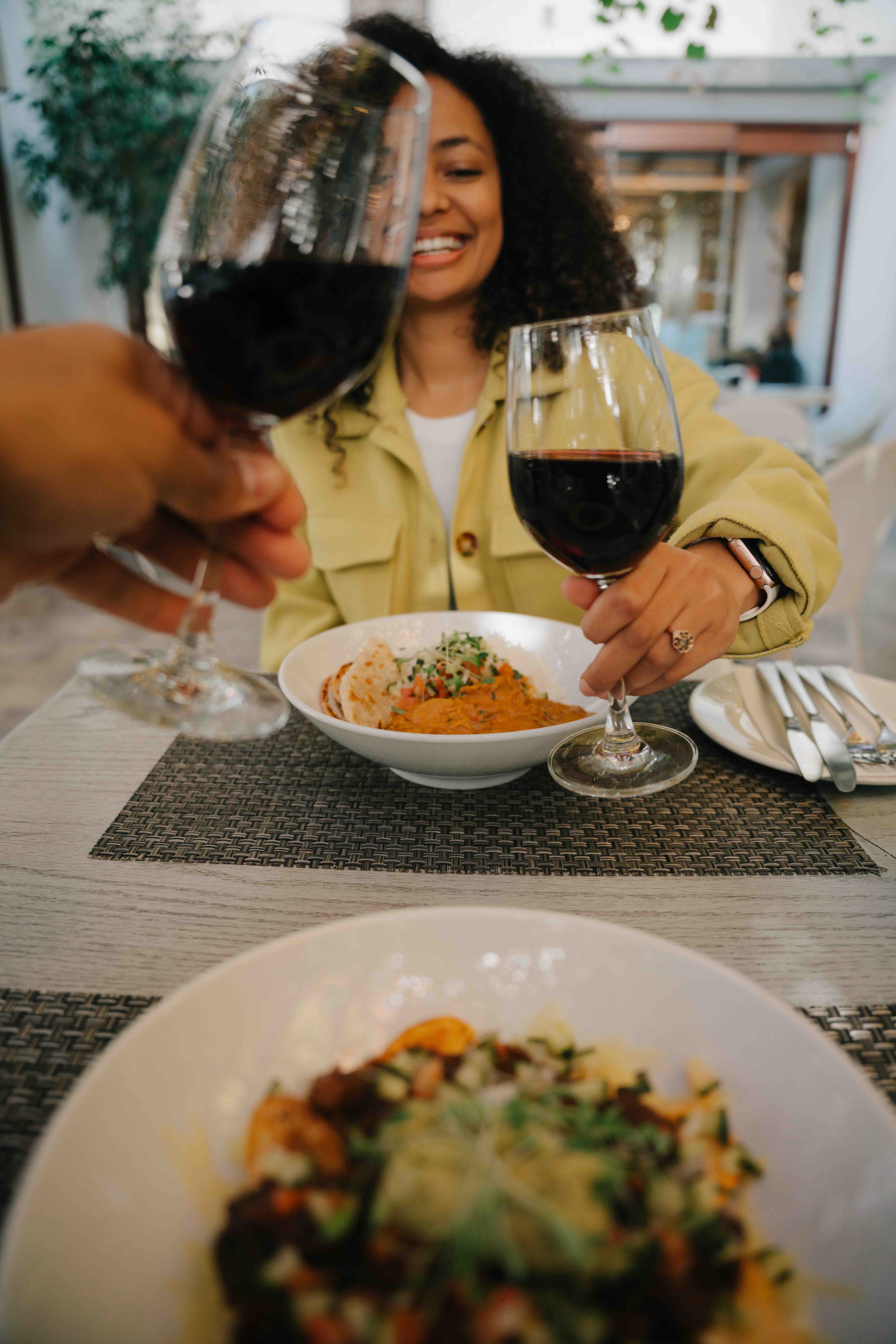 Woman toasting with a glass of red wine at a restaurant, smiling across the table.